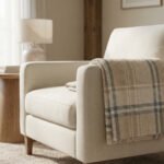 Fauteuil moderne beige avec plaid écossais beige et bleu drapé sur l'accoudoir, dans un salon lumineux. Ambiance chaleureuse.