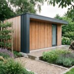 Abri de jardin moderne en bois et gris, jardin paysager luxuriant avec homme jardinant près de plantes et chemin de gravier.