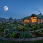 Maison en pierre avec grand jardin en permaculture en spirale sous une pleine lune dans un paysage vallonné.