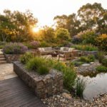 Jardin luxuriant au coucher du soleil avec terrasse en bois, escalier, salon extérieur, murs gabion, bassin naturel et fleurs.