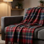 Plaid tartan rouge, vert et bleu sur un canapé gris dans un salon confortable avec cheminée et tasse fumante.