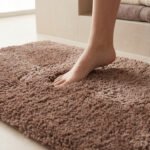 Pied nu posé sur un tapis de salle de bain en fibres douces et marron dans une salle de bain moderne.