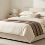 Lit moderne avec parure crème et jeté beige dans une chambre lumineuse et minimaliste.