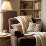 Un fauteuil marron confortable avec un plaid, une lampe sur pied et une petite table basse près d'une bibliothèque.