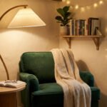 Un fauteuil vert confortable avec un plaid, une lampe sur pied, une table basse avec un livre et une étagère à livres.