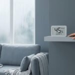 Une main effleure un hygromètre numérique affichant 45% d'humidité près d'une fenêtre couverte de condensation.