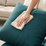 Mains nettoyant un coussin d'extérieur bleu sarcelle avec un chiffon en microfibre beige.