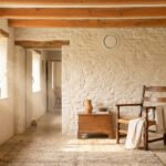 Intérieur rustique avec murs en pierre, poutres apparentes et bouche de ventilation discrète intégrée au mur.