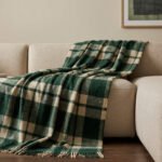 Plaid à carreaux vert et beige drapé sur un canapé beige dans un salon cosy.