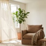 Salon lumineux avec rideaux en lin clairs, un fauteuil confortable et une plante verte pour créer de la fraîcheur.