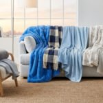 Salon lumineux avec un canapé et un fauteuil ornés de plaids de différentes textures et nuances de bleu.