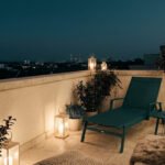Balcon de ville la nuit éclairé par des lanternes et guirlandes lumineuses, avec un transat et des plantes en pots.