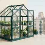 Une petite serre de jardin verte installée sur un balcon urbain avec des plantes en pot à l'intérieur.