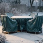 Table et chaises de jardin recouvertes de bâches de protection vertes sous la neige dans un jardin d'hiver.