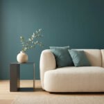 Un salon minimaliste avec un canapé crème, des coussins bleu pétrole et un mur de la même couleur apaisante.
