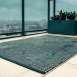Tapis sombre texturé sur un balcon carrelé humide sous une pluie légère avec une jardinière en arrière-plan.