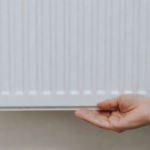 Main sous le bas d'un radiateur blanc, sans outil ni marque.