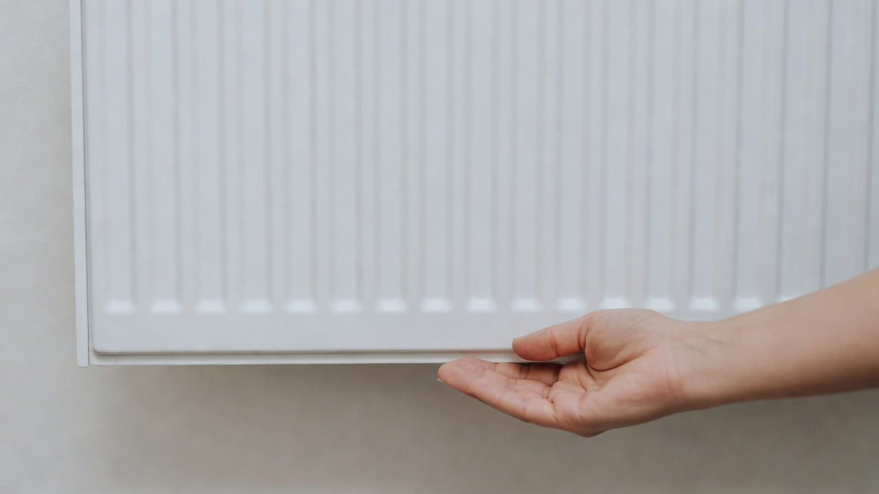 Main sous le bas d'un radiateur blanc, sans outil ni marque.