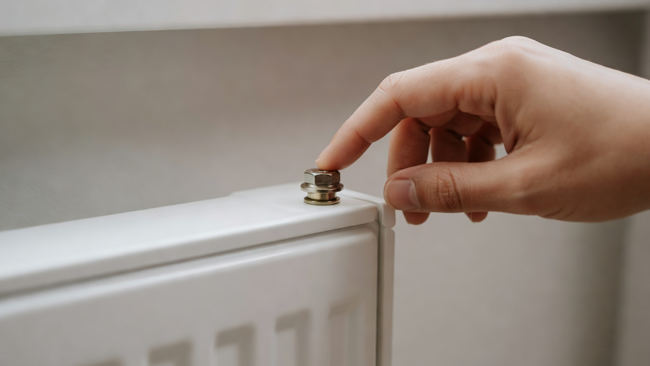 Vis de purge en haut d'un radiateur blanc, main qui ne force pas.